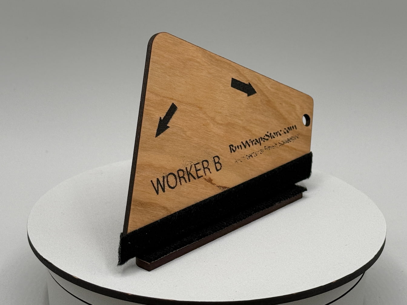 Wooden nameplate with engraved text on a white pedestal against a gray background